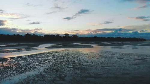 Slow push towards the treeline over an amazingly reflective beach from small veins and bodies of wat