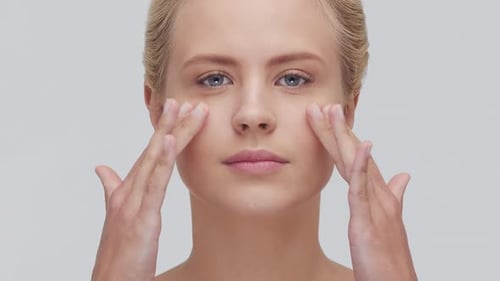 Studio Portrait of Young Beautiful and Natural Blond Woman Applying Skin Care Cream Face Lifting