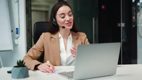 Woman with Headset Signing Contract During Video Call on Laptop in Office