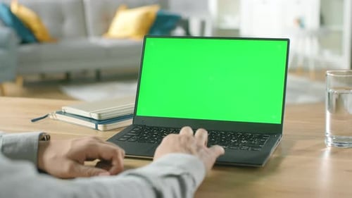 Close-up of a Man Uses Laptop with Green Mock-up Screen While Sitting at the Desk in His Cozy Livin