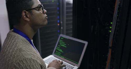 Man Programming on Laptop in Server Room