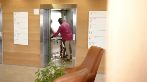 Man in office building elevator holding bicycle, commuting to work