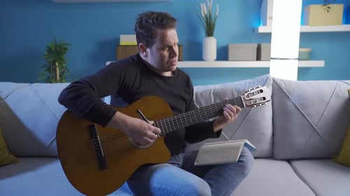 Man Plays Guitar and Writes Music Indoors
