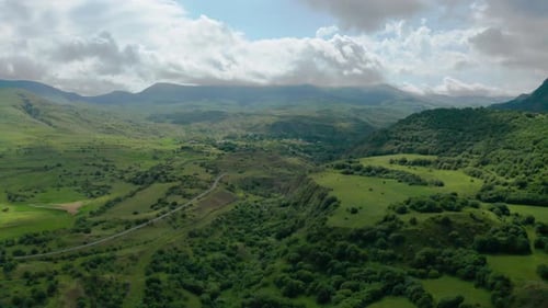 Aerial footage mountains, trees, green grass, clouds.