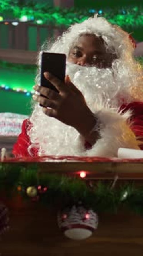 Vertical Video Father Christmas Checking Online Gift Lists on a Tablet in Cozy Festive Workshop