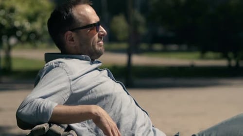 Young man enjoys sunny day relaxing on bench in city park