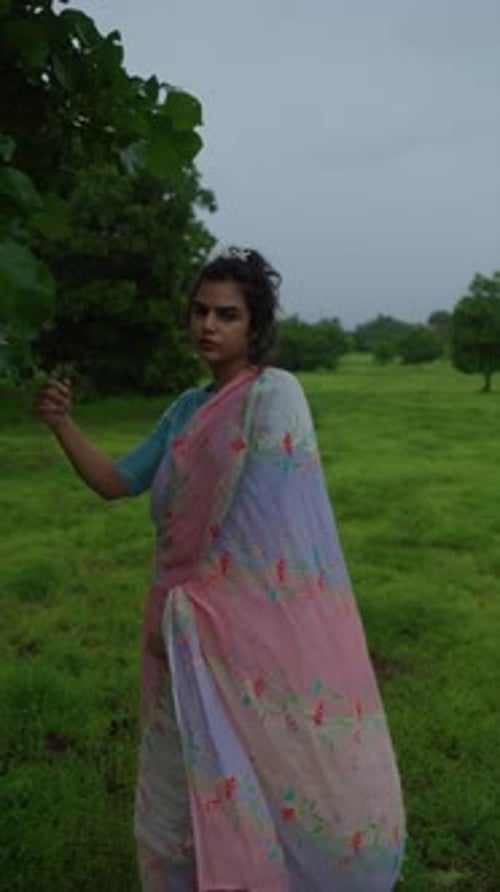 Jeune femme attentionnée dans un paysage rural, portant un sari coloré, serein et réfléchissant