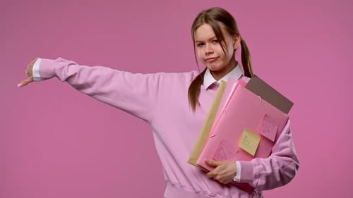 A Young Female Student Gives a Thumbs Down Gesture While Holding Folders and Notes in Her Hands