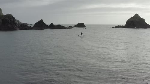 Stand up paddleboarder silhouette in center of frame among ocean rocks