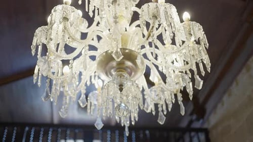 Eleganter Kristall-Kronleuchter mit brennenden Kerzen, der an einer Holzdecke hängt und einen Hauch von Luxus verleiht