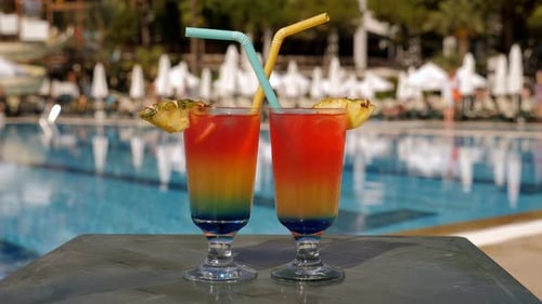 Zwei mehrfarbige Cocktailgläser mit Ananasscheiben und Tuben am Pool