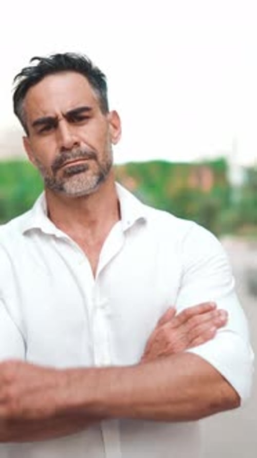 Mature businessman stands with his arms crossed and looks into the camera