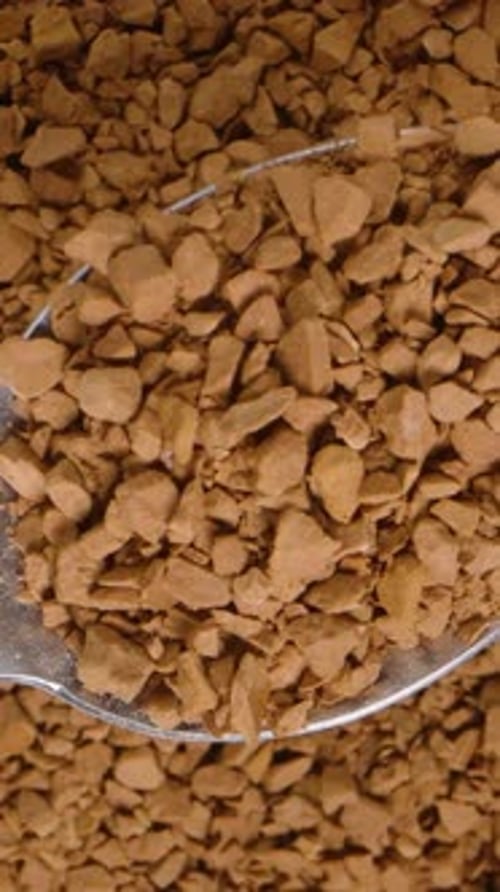 Vertical video. Soluble coffee granules on a metal spoon viewed from above against a background.