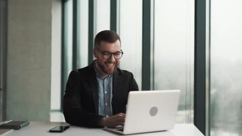 Smiling Man Working at Laptop in Modern Office