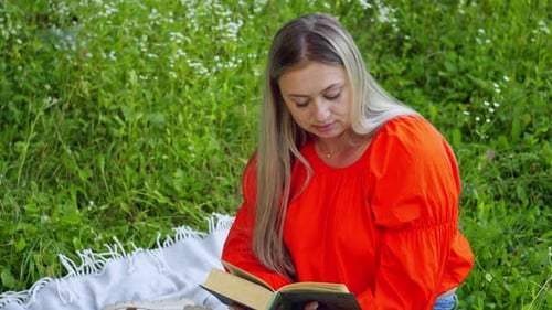 A Woman is Reading a Book While Sitting on a Blanket in the Middle of a Field