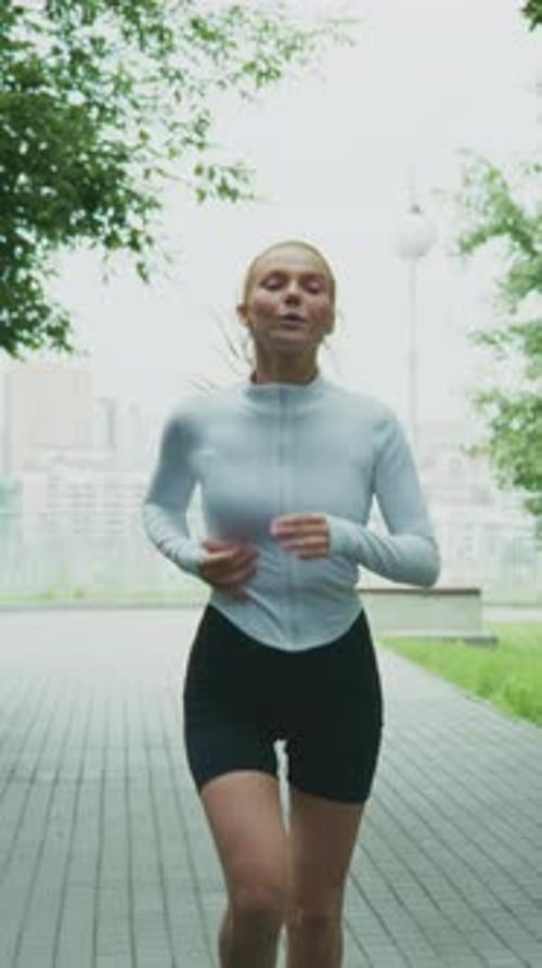 Energetic Female Runner in Activewear Jogging Through a Park Path with Lush Greenery Captivating