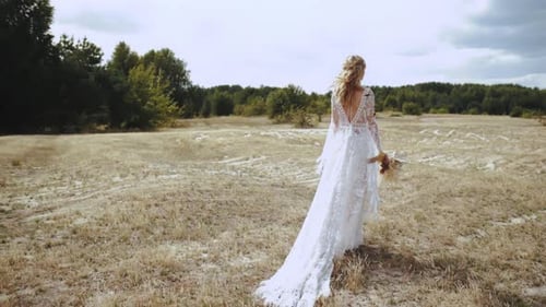 Bride in Wedding Boho Dress Walks Through the Field with a Bouquet Slow Motion Shot