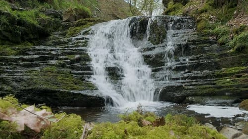 Waterfall in forest 4k slider shot. Showing water running over the rocks with moss and trees in the