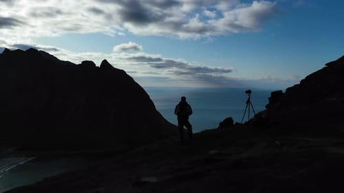 Silhouette of a photographer standing on a mountaintop with a spectacular view of Lofoten island, No