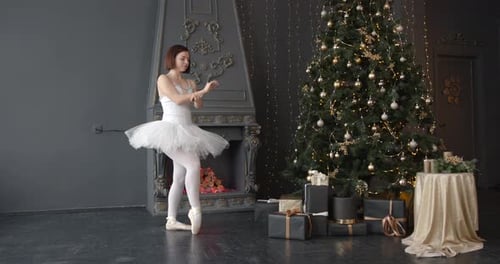 Elegant Ballerina Dances by Christmas Tree in Studio