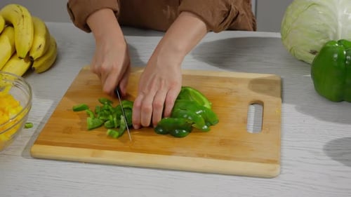 Person dicing green bell pepper on cutting board