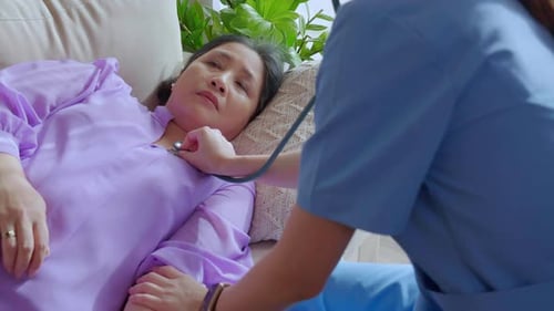 Nurse or caregiver holding stethoscope listen heartbeat with patient senior woman lying on sofa.