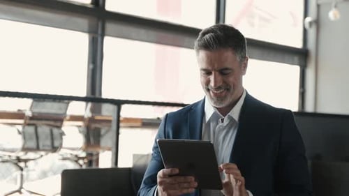 Happy Mature Business Man Wearing Suit Standing in Office Using Digital Tablet
