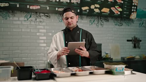 A pensive sushi chef with a tablet in his hands looks at recipes for delicious rolls and ingredients