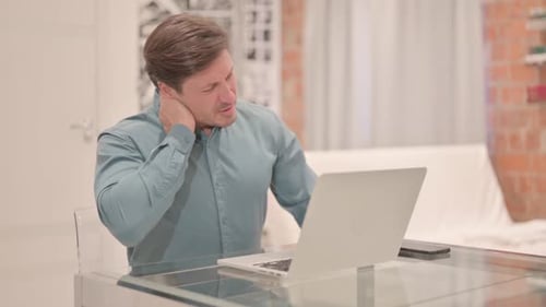 Man Massaging Stiff Neck While Working On Laptop