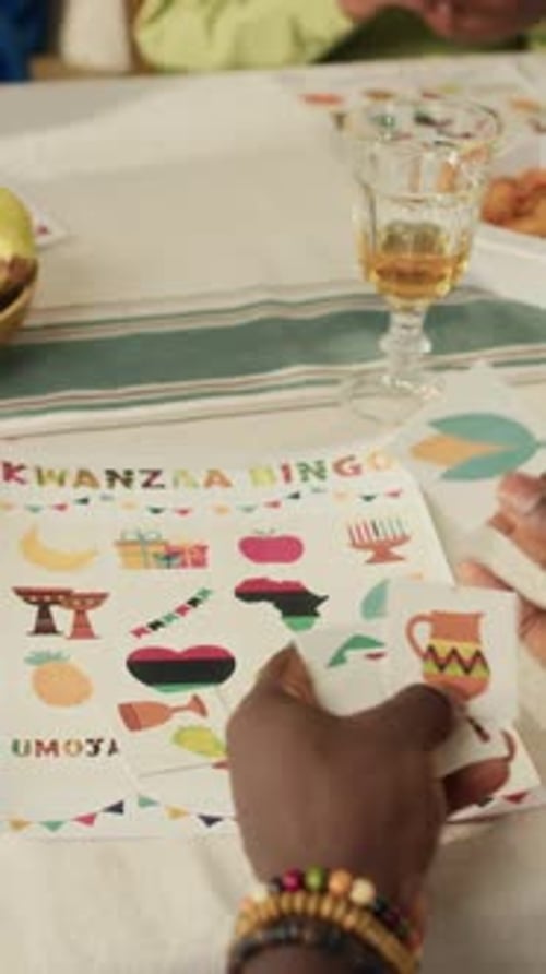 Hands of Man Putting Card on Colourful Activity Sheet Playing Kwanzaa Bingo