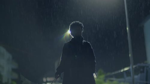 Person Standing Under Umbrella in Heavy Rain at Night