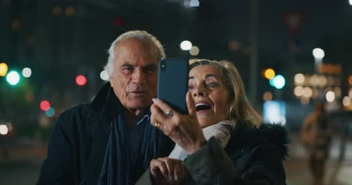 A happy senior couple is making a selfie or video call with a smartphone in a city center in the e