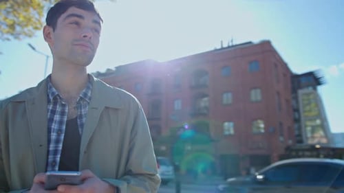 Young Man Typing Text Message on Phone and Looking Around at City Street
