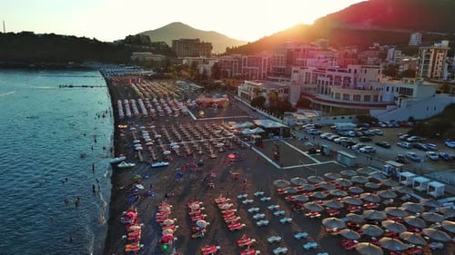 Beach with Sun Umbrellas Sunbeds and People Relaxing in the Town of Becici Near Adriatic Sea Against