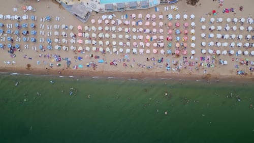 Luftaufnahme eines malerischen Strandes mit Sonnenschirmen und Menschen, die einen sonnigen Tag am Meer genießen