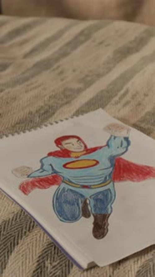 Vertical of Sketchbook with Superhero Pencil Drawing on Child Bed