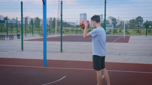 A Guy Practicing on an Outdoor Sports Court with a Basketball
