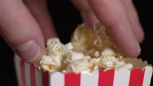 Extreme close up: Caucasian hand reaches into small container of fresh popcorn.