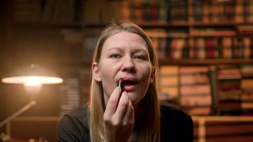 Junge Frau drinnen mit Büchern von hinten malt ihre Lippen mit rotem Lippenstift Ein Mädchen geht auf einen