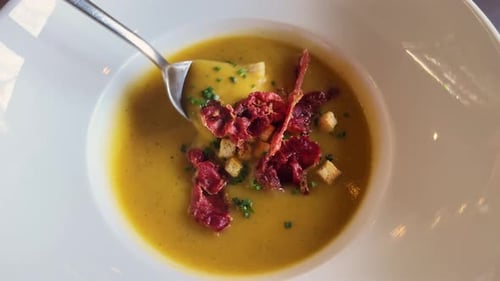 Vegetable Cream Soup with Jamon Herbs and Croutons on a Wooden Table in a Restaurant