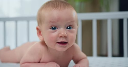 Close up. Portrait of beautiful infant kid is lying on the white bed on his stomach. A nice little