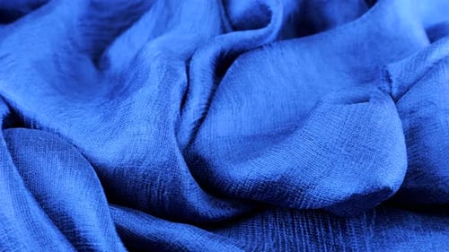 Close-up view of soft folds of dark blue silk muslin rotated on the display case. Textile background
