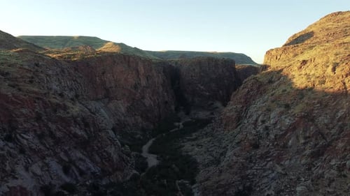 Cinematic aerial view flying over a lush desert gorge between two cliffs at golden hour at riemvasma