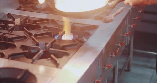 The chef prepares the dish on the stove with an open fire in the kitchen of the restaurant.
