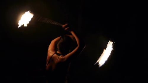 Asian spinning fire poi in large circular motion during night, filmed from backside as medium shot