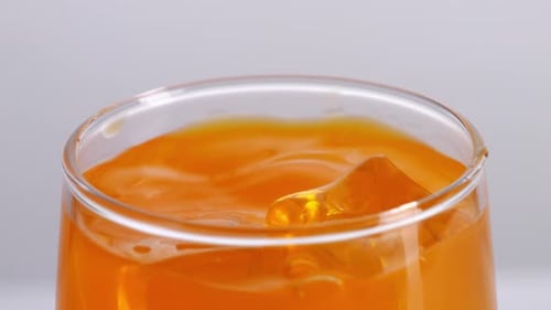 Close Up Of Ice Cubes Falling In A Glass Of Orange Juice On The Light White Screen Background