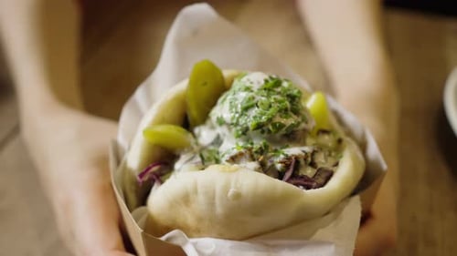 Female Hands Slowly Turn Delicious Falafel in Pita with Sauce and Cucumbers