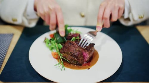 Woman cutting a medium rare steak served with vegetables and sauce on a restaurant plate
