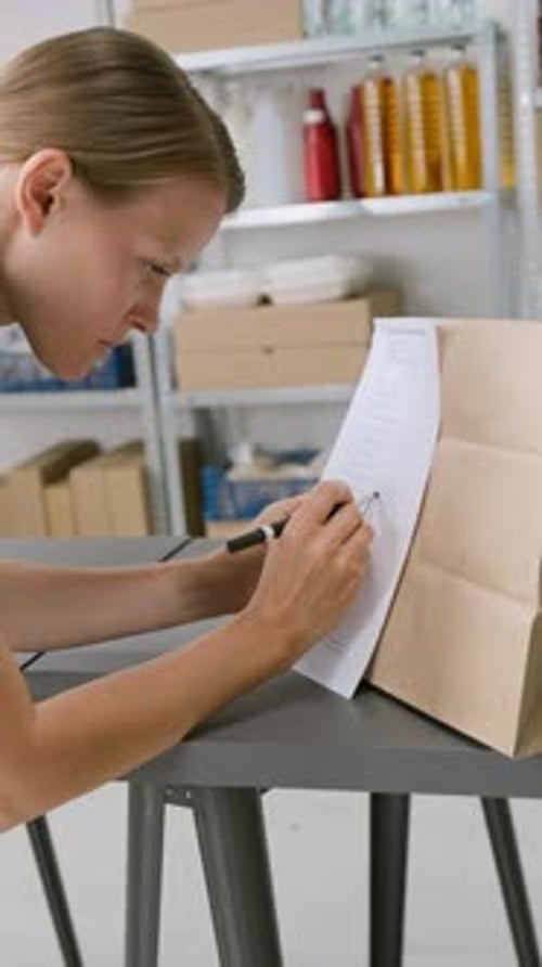 Female Worker Writing Date on Order Invoice at Dark Grocery Store