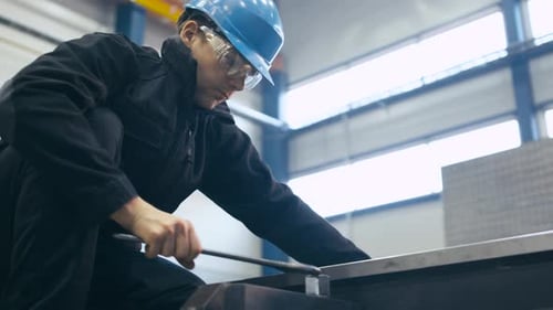 Industrial worker is tightening screws with a wrench at a factory.
